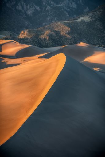 A vertical shot of sand dunes with mountains in the background at daytime