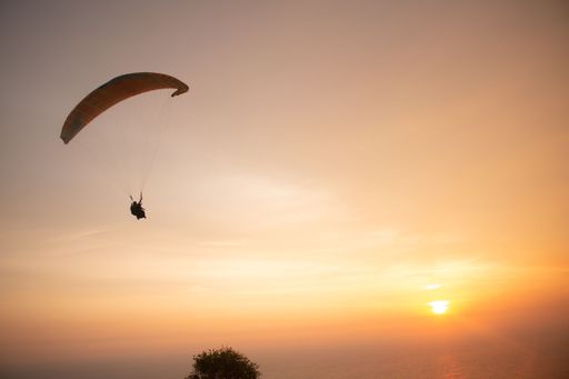 Tandem paragliding over the ocean while golden sunset at Parangtritis beach on Java island in Indonesia.