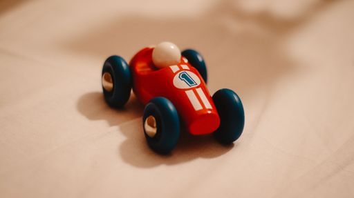 A toy car with the number 1 on it. A red car with blue wheels on beige surface.