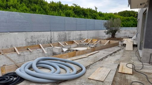 A construction site with wooden materials, pipes, and hoses with green trees in the background