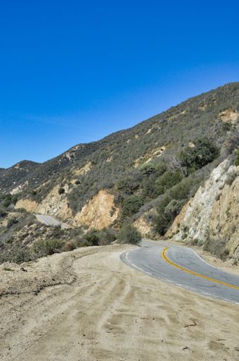 A vertical shot of road surrounded by greenery hills under blue bright sky