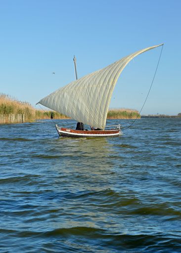 A vertical shot of people behind the white sail of the boat in blue lake