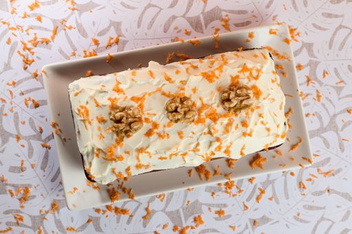An overhead shot of a carrot cake with almonds and nuts in a plate on a white table