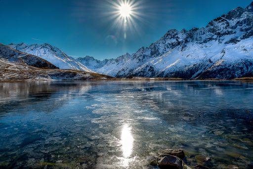A breathtaking shot of a beautiful frozen lake surrounded by snowy mountains during a sunny day