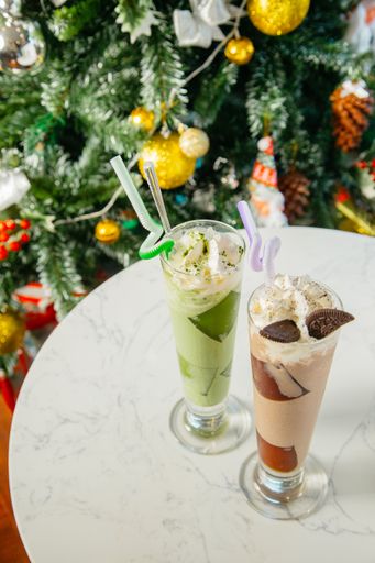A high angle vertical shot of two glasses of cocktail with cream and chocolate with the beautiful Christmas tree in the background