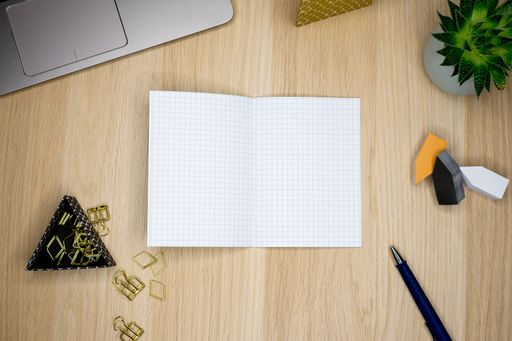 A top view of an open squared notebook on a cluttered wooden office desk