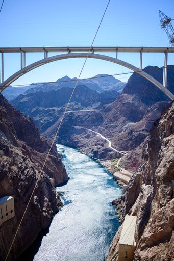 A vertical shot of a long river flowing in the mountains under the Hoover Dam Bridge