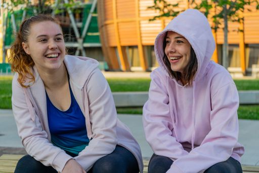 Two caucasian women sitting on stone talking and happily smiling - the concept of friendship