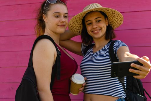 Two young caucasian women smiling and doing a selfie together with a magenta wall on the background