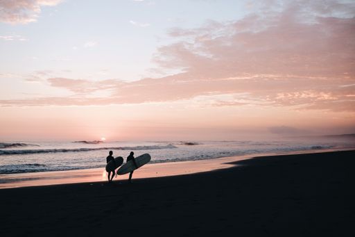 A silhouette of two surfers carrying their surfboards at the seashore during sunset
