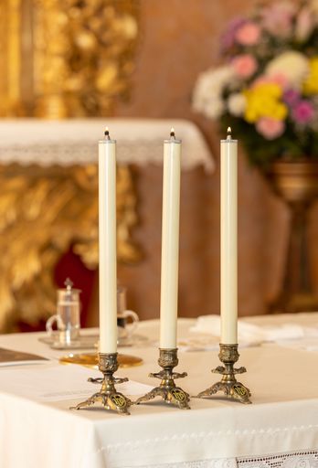A vertical shot of a candlestick with three candles on altar in church
