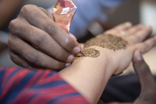 A closeup shot of a male drawing on a female's hand with brown henna