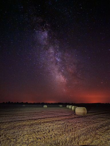 A vertical shot of round hay bales in a field under a beautiful night sky with the Milky Way