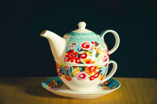 A close-up of a teapot and cup with beautiful floral pattern on a black background