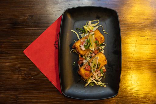 A high angle shot of fried mozzarella sticks with lime and salad in a black plate on the table