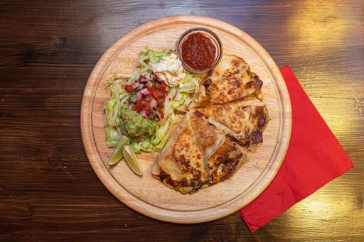 A closeup shot of delicious mexican quesadilla with grilled cheese, salad and lime on a wooden tray