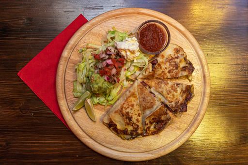 A closeup shot of delicious mexican quesadilla with grilled cheese, salad and lime on a wooden tray