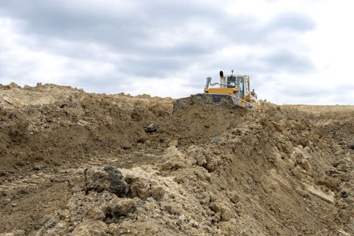 A bulldozer moving soil and rocks at a construction site against a cloudy sky