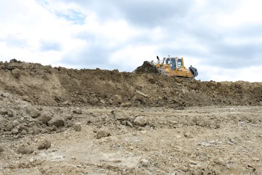 A bulldozer on a mound of soil and rocks at a construction site against a cloudy sky