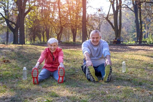 Active senior male and female exercising in the park in autumn