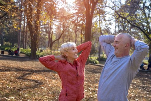 A senior couple stretching in a park happily during daylight