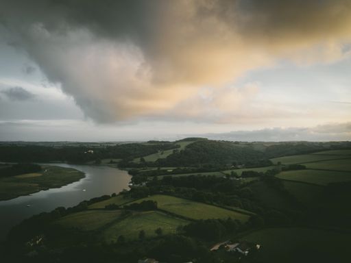 An aerial shot of a calm river surrounded by green nature and hills