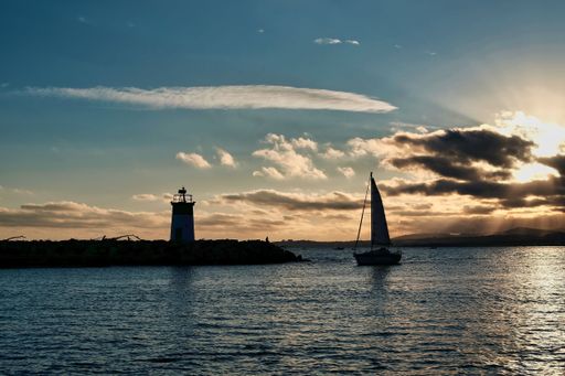 A beautiful scene of a silhouetted sialing boat  on the sea and a lighthouse against a dark sunset sky