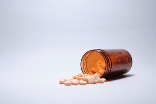 A closeup shot of pink tablets fallen out brown bottle on white background