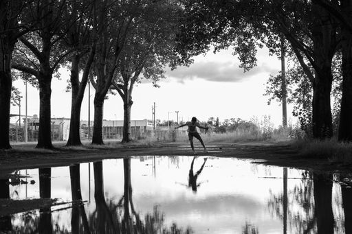 A Caucasian kid jumping over a pond in a park in grayscale