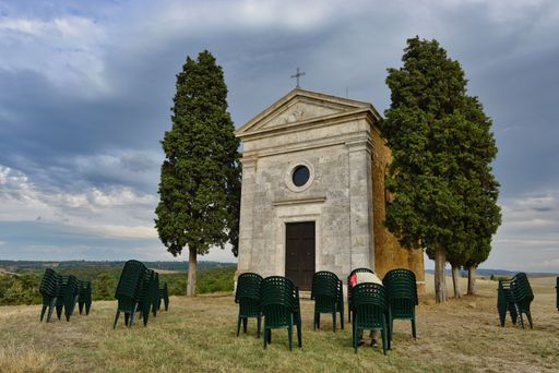 A beautiful shot of the Chapel of the Madonna di Vitaleta with stacked plastic chairs in the front
