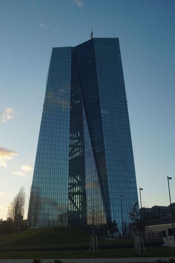 Silhouette of the European Central Bank in Frankfurt, Germany in winter evening light. A glass monolith against a blue sky.