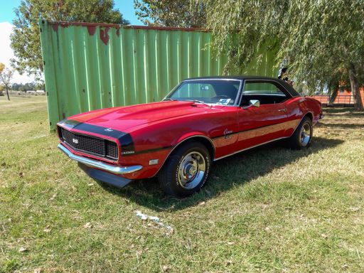 Old red sport Chevrolet Camaro SS 396 coupe First Generation late 1960s by GM parked on the grass. Classic muscle car.