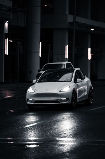 A vertical closeup of a white Tesla driving on the pet roads in the streets