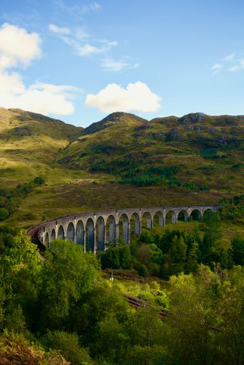 A vertical shot of the Glenfinnan railway Viaduct surrounded by green area with forests and mountains