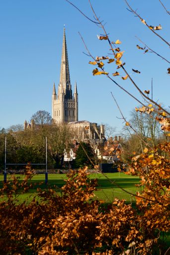 A vertical shot of the Norwich castle seen behind the autumn trees under the blue sky, UK