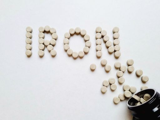 From the inverted jar, iron supplement pills come out onto the white surface of table, forming the inscription iron. Top view