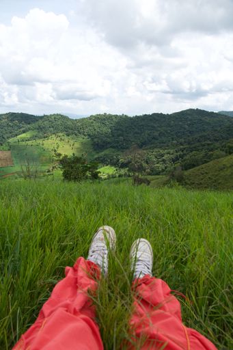 A vertical shot of the woman's legs sitting on the grass with beautiful hills in the background