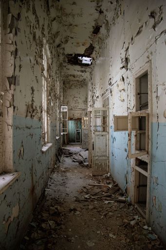 An empty corridor of an abandoned building with damaged walls, doors and windows