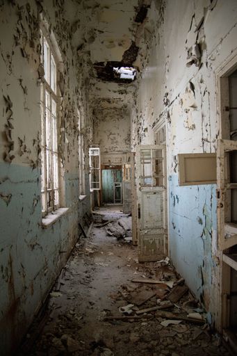 An empty corridor of an abandoned building with damaged walls, doors and windows