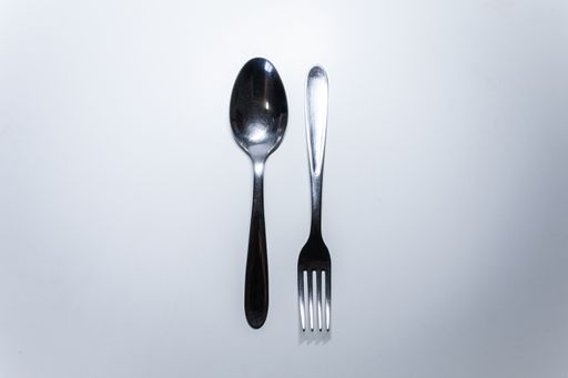 A top view of a silver fork and spoon on a white surface with copy space