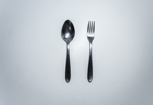 A top view of a silver fork and spoon on a white surface with copy space