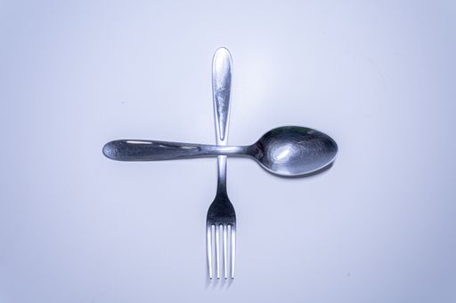 A top view of a silver fork and spoon on a white surface with copy space