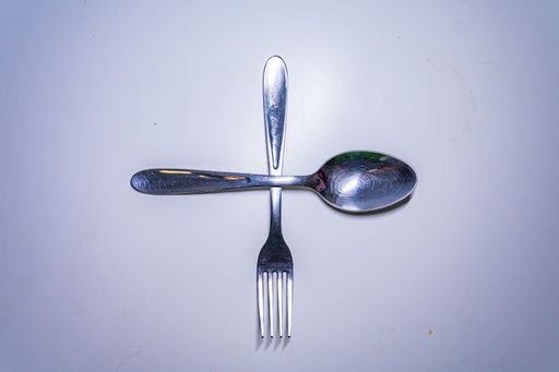 A top view of a silver fork and spoon on a white surface with copy space