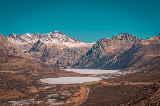 A picturesque view of a frozen mountain lake surrounded by rocky hills and mountains on blue sky background