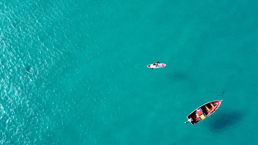 An aerial top view of a surfer on their board and a boat sailing in the blue seascape on a sunny day