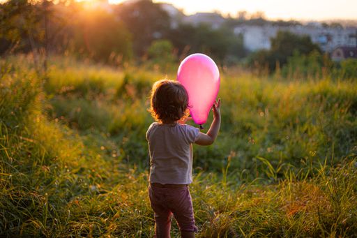 A little child holding a balloon while standing in the middle of a grass-covered meadow