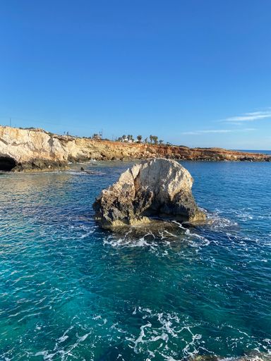 A vertical shot of the rock on the water surface against the blue sky.