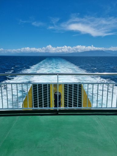 A vertical shot of a boat sailing in the blue seascape leaving a white trace of foam behind