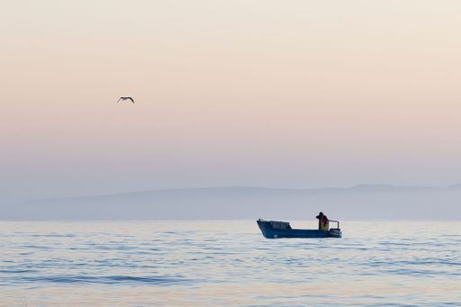 A fisherman on a wooboat catching fish during sunrise.