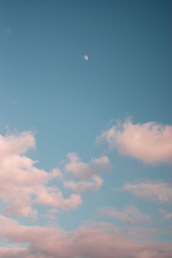 A vertical shot of clouds and moon in a blue sky at sunset